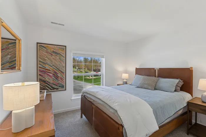 Charming bedroom at ReNew Howard Crossing with a plush bed, elegant artwork, and a scenic view through a large window.