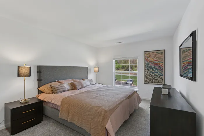 Bright and inviting bedroom at ReNew Howard Crossing featuring a comfortable bed with stylish linens, elegant bedside lamps, and large windows allowing natural light to fill the space.