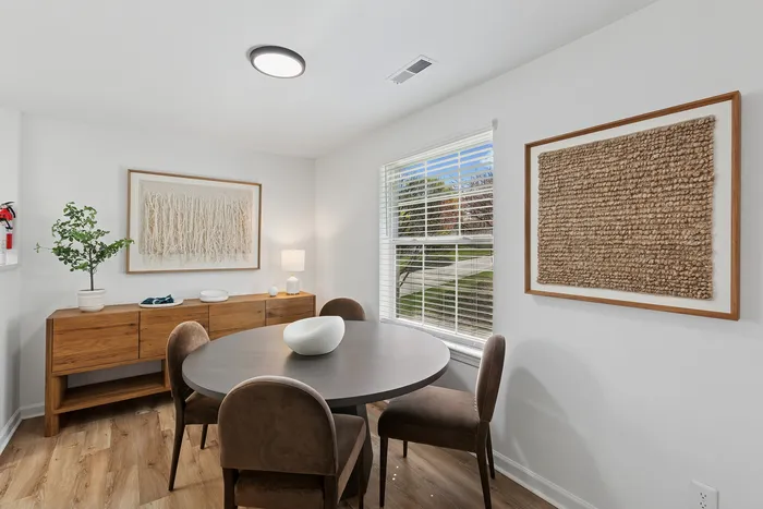 Inviting dining area at ReNew Howard Crossing with a round table, stylish wooden sideboard, and natural light streaming through wide windows, complemented by modern wall art.