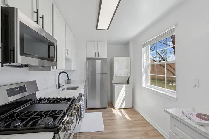 Modern kitchen at ReNew Howard Crossing featuring sleek stainless steel appliances, ample cabinetry, and in-unit washer and dryer under natural light.