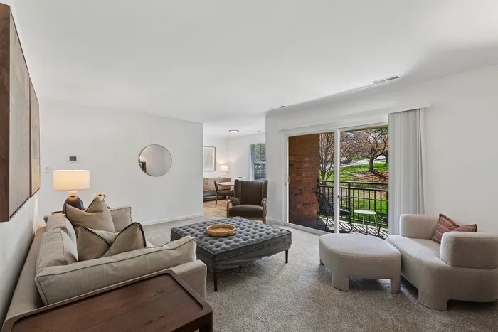Inviting living room at ReNew Howard Crossing with plush seating, elegant d&eacute;cor, and sliding glass doors opening to a serene balcony view.