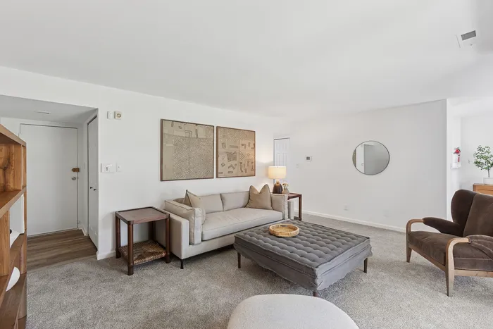 Inviting living room at ReNew Howard Crossing with modern decor, featuring a cozy beige sofa, plush ottoman, and warm lighting, perfect for relaxation.