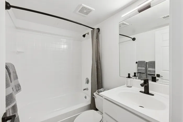 Modern bathroom at ReNew Howard Crossing showcasing a sleek white design, featuring a bathtub with a stylish curved shower rail, and elegant black fixtures.