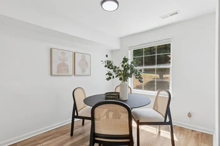 Bright and modern dining area at ReNew Howard Crossing  with a round table, chic chairs, and elegant artwork, filled with natural light coming through a large window.