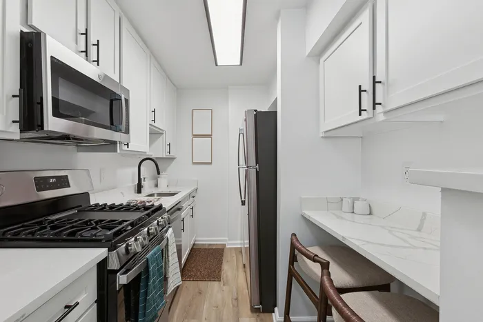 Sleek minimalist kitchen at ReNew Howard Crossing with modern stainless steel appliances and elegant white cabinetry, featuring a cozy breakfast nook and stylish decor.