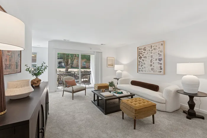 Bright and welcoming living room at ReNew Howard Crossing with modern decor, plush carpeting, and a sliding glass door leading to an outdoor patio.