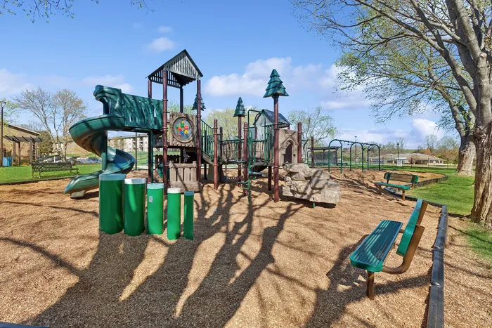 Inviting playground at ReNew Howard Crossing with green slides, adventurous climbing structures, and a serene park setting, perfect for family fun and outdoor activities.