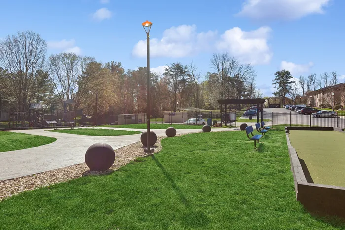 Vibrant outdoor community area at ReNew Howard Crossing featuring a lush green lawn, walking paths, modern playground, and ample seating surrounded by natural beauty.