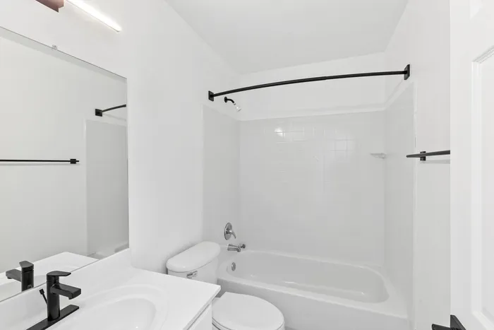 Contemporary bathroom at ReNew Howard Crossing with sleek black fixtures, pristine white tiles, and a bathtub, offering a modern and fresh design.