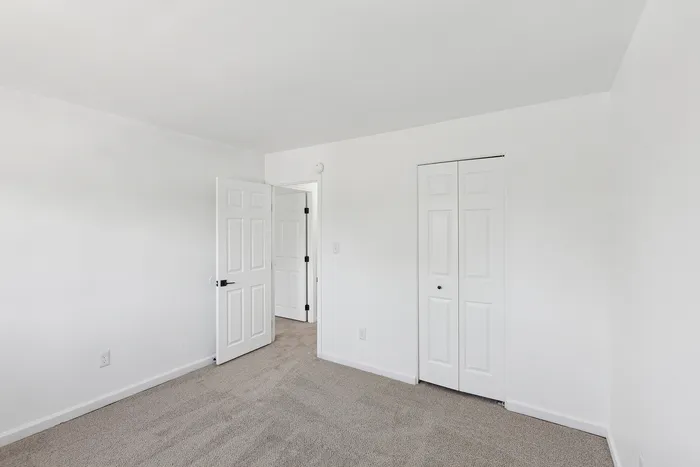 Bright and inviting bedroom at ReNew Howard Crossing with fresh white walls, cozy carpeted floor, and ample closet space, offering a blank canvas for personalization.