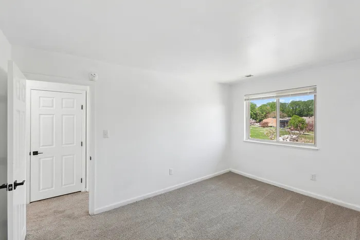 Bright and airy bedroom at ReNew Howard Crossing with plush carpet, large window with picturesque view, and modern white door.