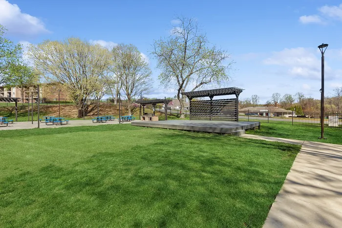 Spacious community outdoor area at ReNew Howard Crossing with vibrant green lawn, modern pergola, and picnic tables perfect for gatherings.