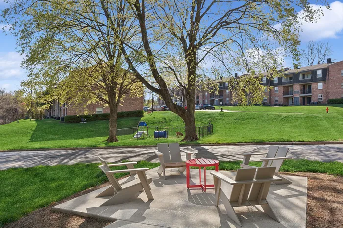 Charming community courtyard at ReNew Howard Crossing with cozy seating area under lush trees, perfect for relaxation, with brick apartments in the backdrop and vibrant greenery all around.