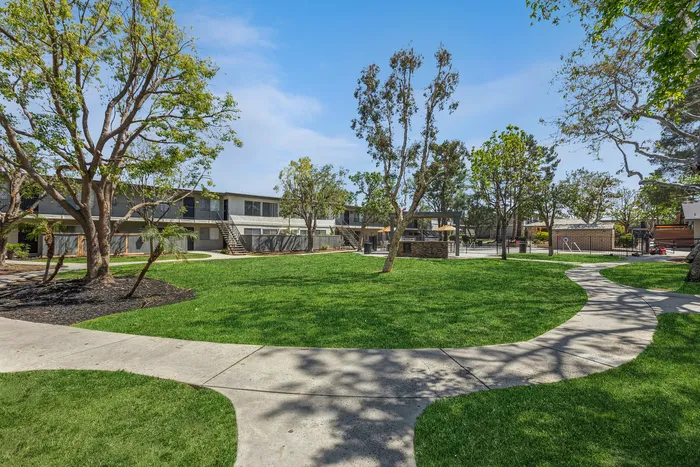 Charming apartment complex surrounded by lush greenery and meandering walkways under a clear blue sky.