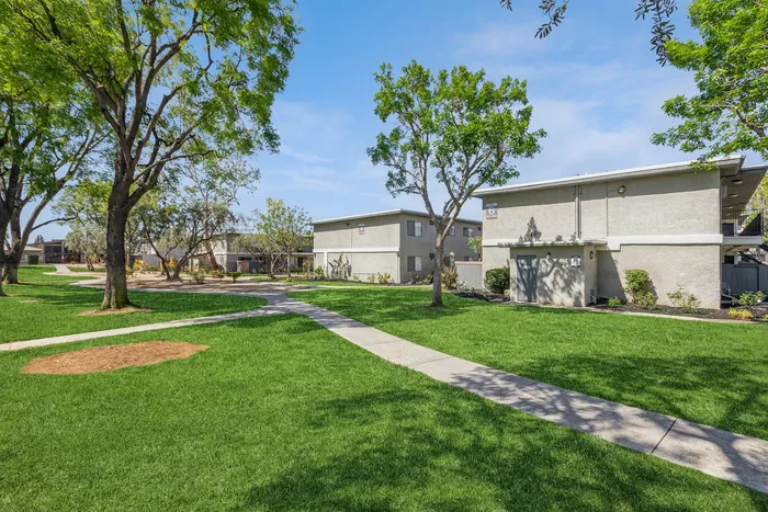 Charming outdoor view of modern apartment buildings surrounded by lush green lawns and mature trees, offering a serene and welcoming community atmosphere.