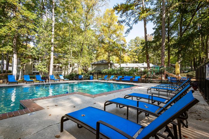 Inviting outdoor pool area with blue loungers, surrounded by lush greenery and a serene forest backdrop, perfect for relaxation and leisure.