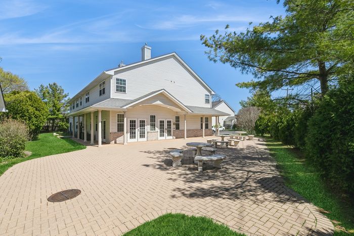 Charming two-story building with expansive outdoor patio, lush greenery, and inviting seating area under a clear blue sky.