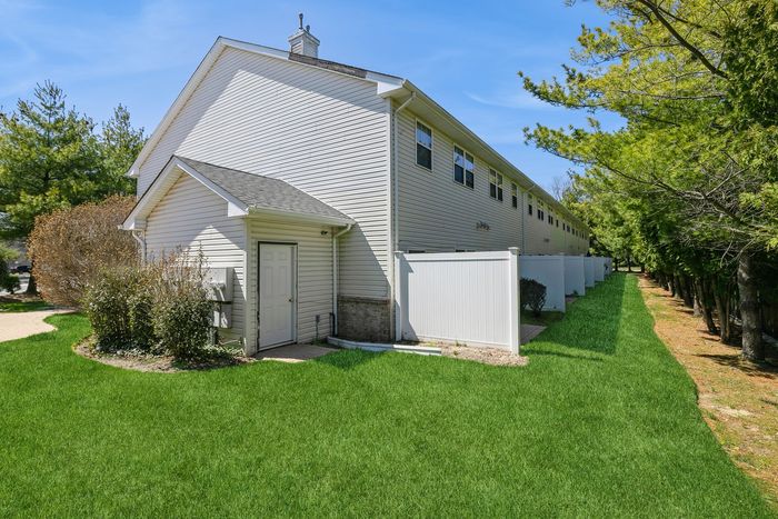 Charming townhouse exterior featuring lush green lawn and white privacy fencing under a clear blue sky.