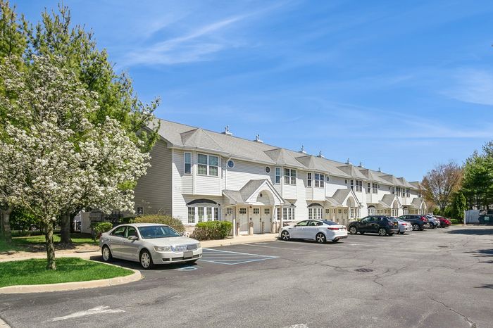 Charming townhouse community with blossoming trees, ample parking, and sunny blue skies.