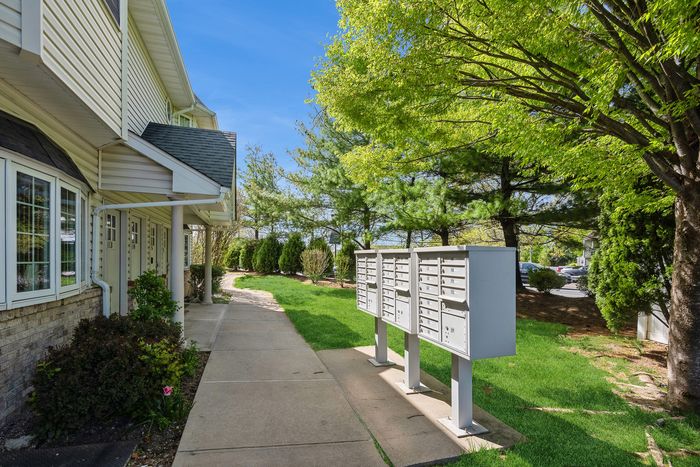 Charming residential walkway with lush greenery and convenient mailbox stations, leading to welcoming apartment entrance.