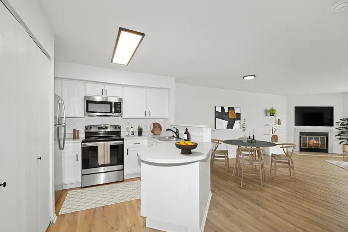 Bright and modern open-concept kitchen and dining area with sleek appliances and stylish wooden flooring, featuring a cozy fireplace and elegant decor.
