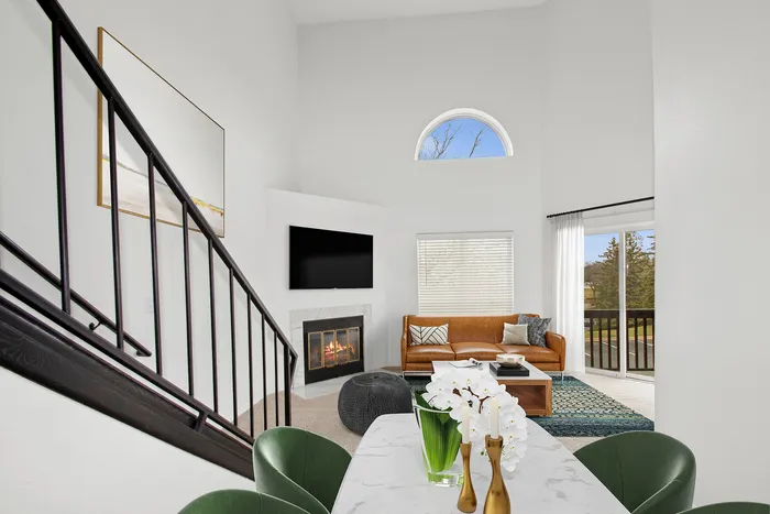Modern living room with a high ceiling showcasing a cozy fireplace, stylish brown leather sofa, and elegant decor with natural light streaming through large windows.