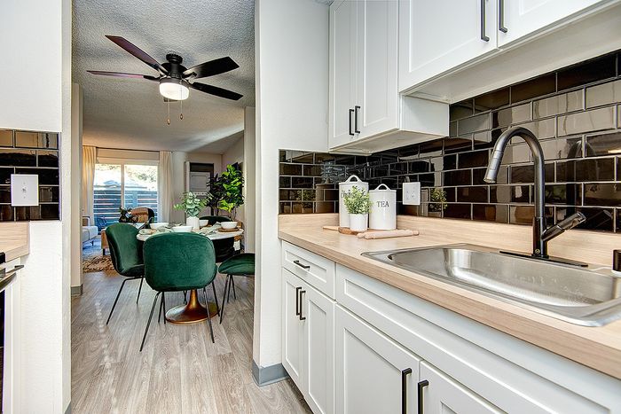 Contemporary kitchen with sleek black tile backsplash, white cabinets, and a cozy dining area with green chairs at ReNew Dash Point.