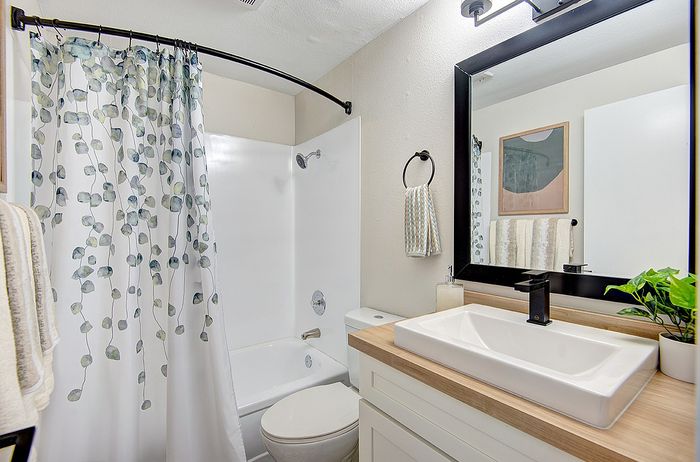 Bright and modern bathroom featuring a chic shower curtain with leaf patterns, stylish vanity with black accents, and a touch of greenery for a fresh ambiance at ReNew Dash Point.