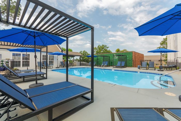 Inviting poolside paradise with stylish lounge chairs, vibrant blue umbrellas, and modern pergolas under a sunny sky.