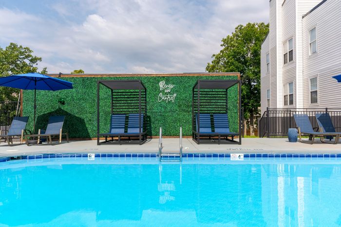 Inviting poolside area with modern cabanas and vibrant green wall at Renew on Caney, perfect for relaxation.