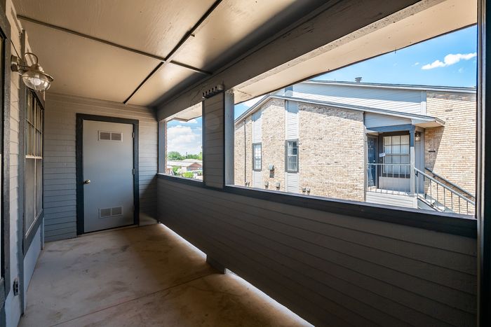 Charming apartment patio with modern design, featuring ample space and a view of neighboring buildings under a bright blue sky.