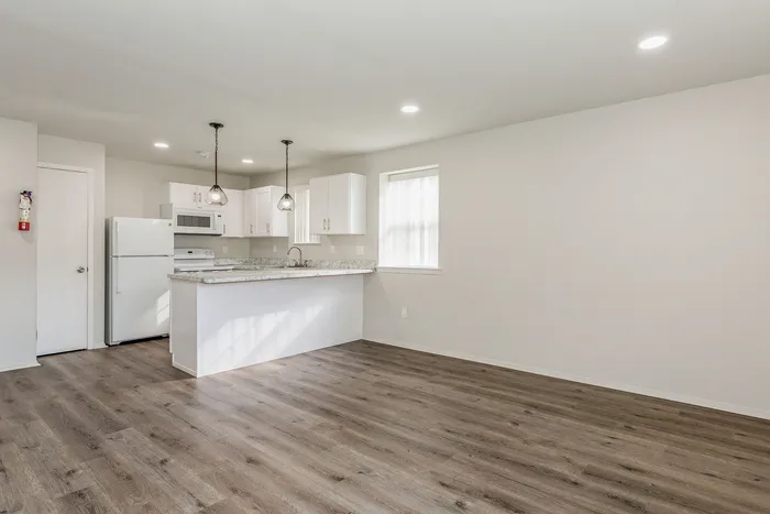 Modern open-concept kitchen with sleek white cabinetry, marble countertops, and elegant pendant lighting on hardwood floors.