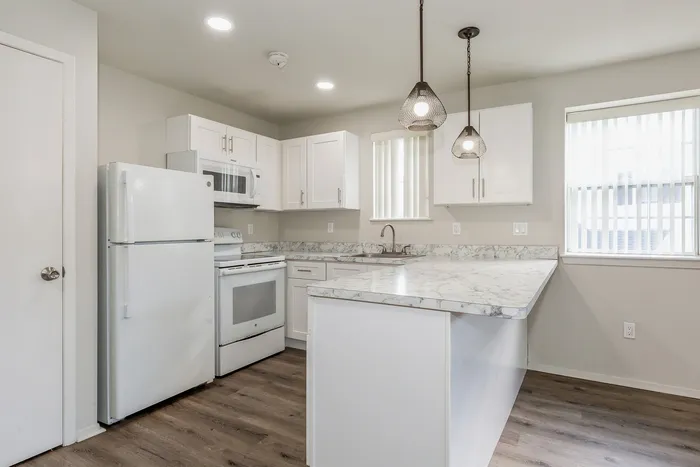 Modern kitchen with sleek white cabinetry, marble countertops, and stylish pendant lighting, perfect for culinary adventures.