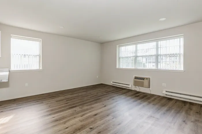 Bright and airy living room with large windows, sleek wood flooring, and modern wall-mounted air conditioning unit.