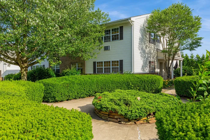 Charming two-story home with elegant landscaping surrounded by lush greenery and a welcoming pathway.