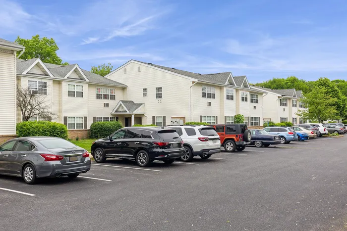 Charming suburban apartment complex with ample parking and lush green surroundings, perfect for comfortable living.