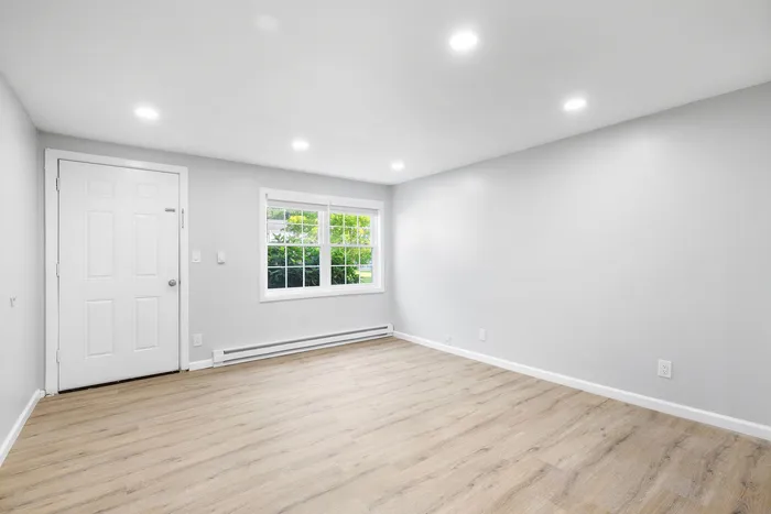 Bright and inviting living space with modern wood flooring, large window, and soft recessed lighting.