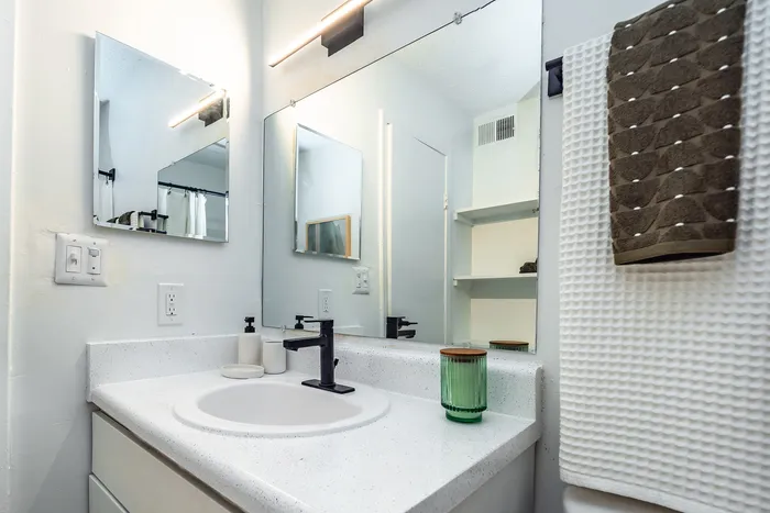 Modern bathroom featuring a sleek white countertop, stylish black faucet, contemporary lighting, and tasteful decor.