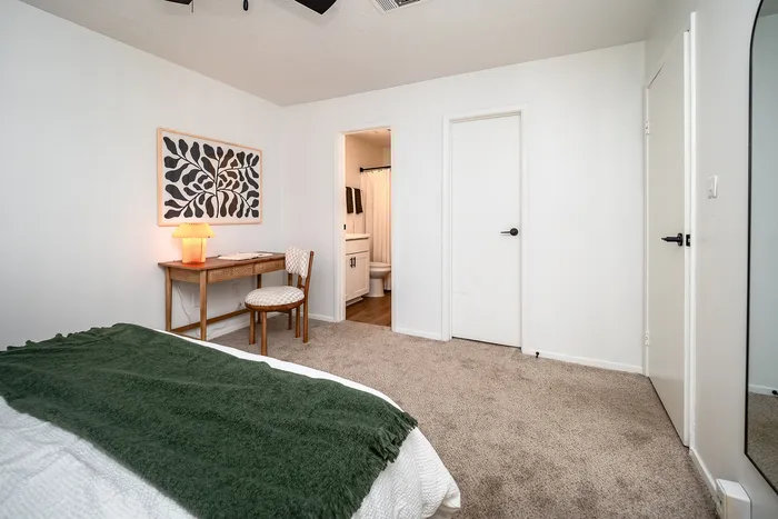 Cozy bedroom featuring stylish desk with modern artwork, plush carpeting, and access to a chic en-suite bathroom.