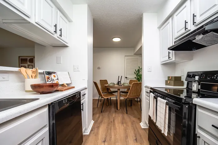 Charming kitchen with sleek white cabinets and modern appliances leading to a cozy dining area with wicker chairs.