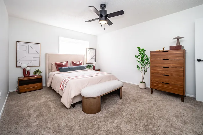 Inviting bedroom with modern decor featuring a plush bed, elegant dresser, and stylish accent pieces, enhanced by natural light and cozy carpet flooring.