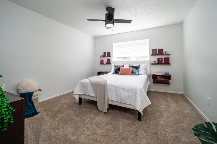 Inviting bedroom with a cozy bed, modern ceiling fan, and elegant wall shelves, creating a serene and stylish ambiance.