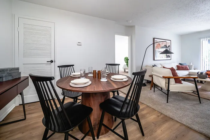 Modern open-concept living space featuring a cozy dining area with a sleek round table, stylish black chairs, and a comfortable lounge area with neutral-toned furniture and vibrant accents.