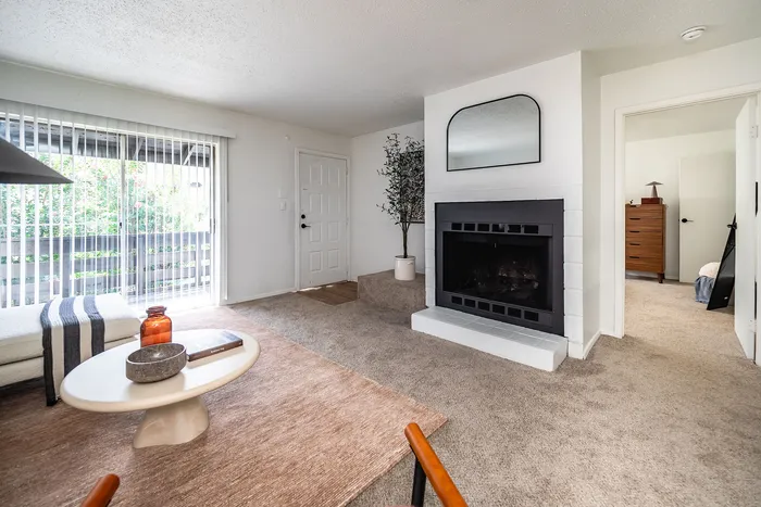 Inviting modern living room with plush carpeting, a sleek fireplace, and abundant natural light from large glass doors.