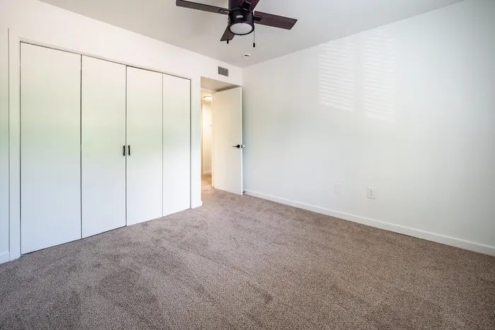 Bright and spacious bedroom with plush carpet and stylish ceiling fan, featuring a large closet with sleek white doors.