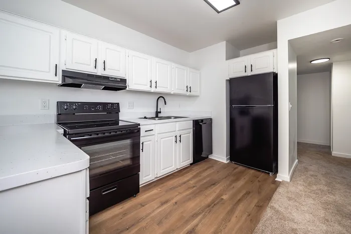 Modern kitchen with sleek black appliances, elegant white cabinetry, and rich wood flooring, offering a sophisticated cooking space.