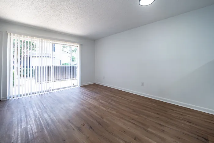 Bright living area with sleek wooden flooring and large sliding glass doors opening to a tranquil outdoor view.