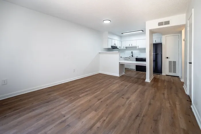 Modern open-plan living area with sleek hardwood floors, showcasing a bright kitchen equipped with white cabinetry and contemporary appliances.
