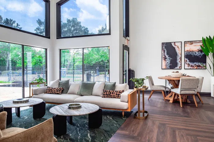 Bright and airy living area with high ceilings, modern furniture, large windows with scenic views, cozy seating, and stylish decor.