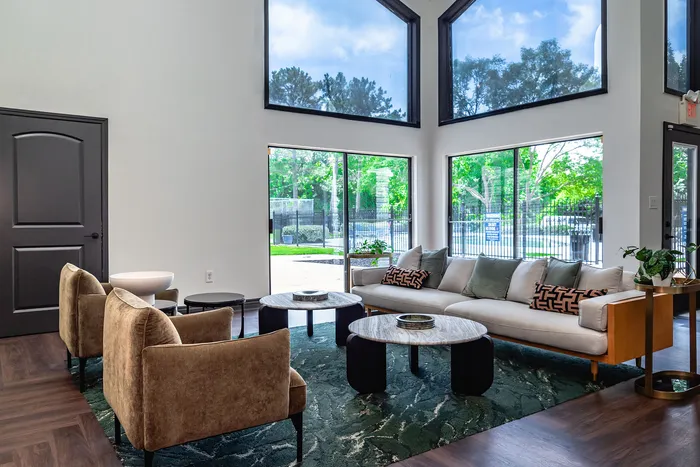 Elegant living room with floor-to-ceiling windows, stylish sofas, and chic marble coffee tables overlooking a lush garden view.